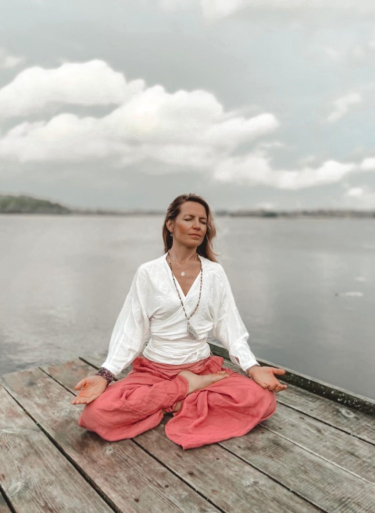 Szczęśliwa kobieta medytuje rankiem nad brzegiem jeziora, medytacja na dobrobyt.