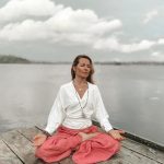 Kobieta siedzi na pomoście i medytuje, joga kundalini.