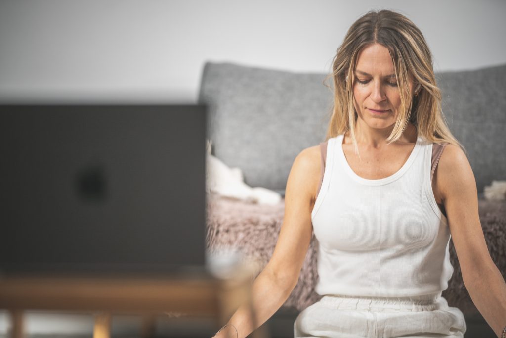 Kobieta praktykuję jogę kundalini online z użyciem komputera.